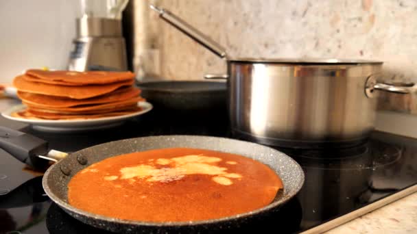 Ένα θηλυκό χέρι χρησιμοποιώντας μια πράσινη σπάτουλα σιλικόνης βάζει βούτυρο σε μια παραδοσιακή ρωσική τηγανίτα, η οποία ψήνεται και ψήνεται σε ένα ταψί. Το βούτυρο λιώνει στη ρωσική τηγανίτα. Μαγειρεύοντας ρωσικές τηγανίτες, κοντινό πλάνο. - Πλάνα, βίντεο