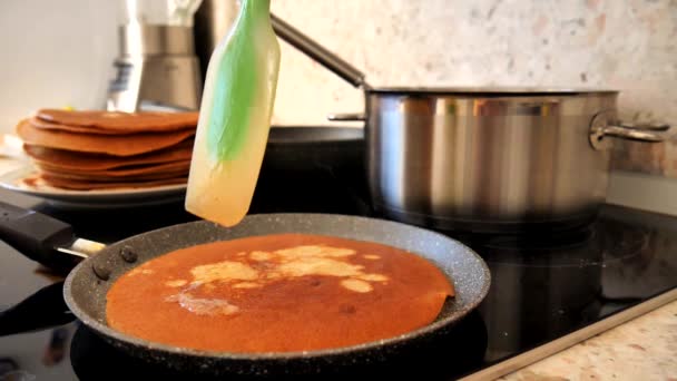 Une spatule de silicone vert étend le beurre sur la crêpe et l'enlève de la casserole. La vapeur de la crêpe monte lentement. Cuisiner des crêpes traditionnelles russes. Gros plan. Mouvement lent
. - Séquence, vidéo