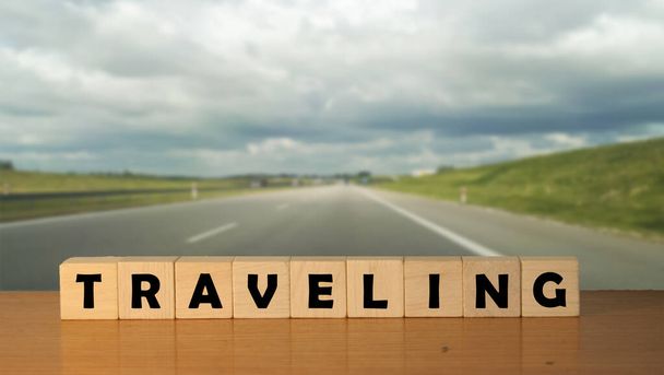 TRAVELING message word on a wooden desk on cube blocks with a empty road backgroun - Фото, изображение
