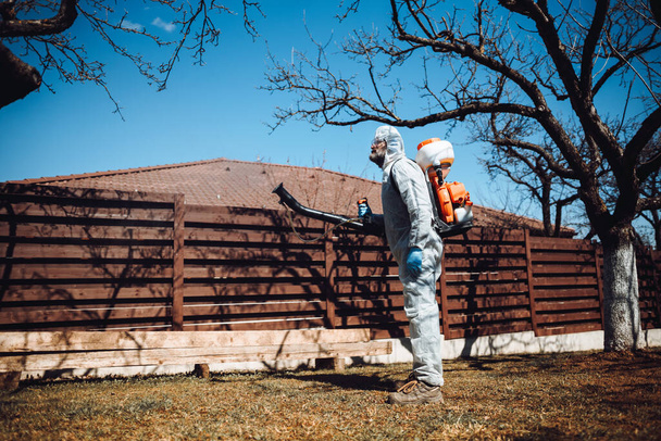 Portrait d'un travailleur masculin portant des vêtements de protection et pulvérisant un insecticide dans un verger fruitier
 - Photo, image