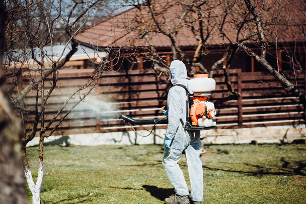 Agriculture worker spraying pesticides in fruit orchard using mistblower and organic chemicals - Foto, Imagem