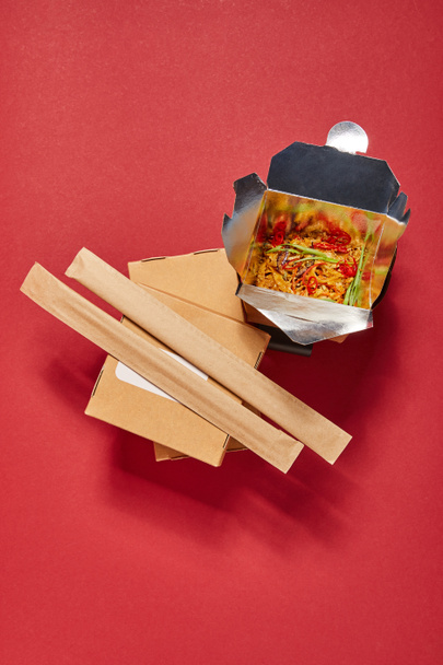 top view of chopsticks in paper packaging near spicy noodles in takeaway box on red - Photo, Image