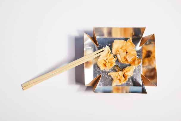 top view of takeaway box with fried dumplings and chopsticks on white  - Fotó, kép