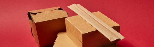 panoramic shot of chopsticks in paper packaging near takeaway carton boxes with chinese food on red - Foto, Imagem
