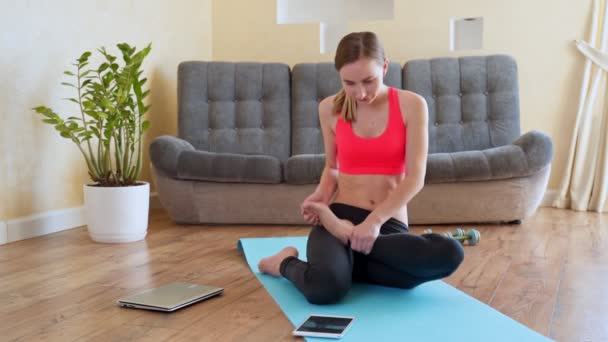 Egy nő laptoppal nézi otthon az online jóga gyakorlatokat. A fiatal nő otthon edz a COVID 19 járvány miatt.. - Felvétel, videó