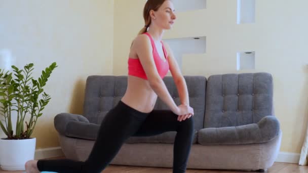 Slim sportswoman in sportswear warming-up muscles before workout doing stretching exercise sitting on floor at home - Filmati, video