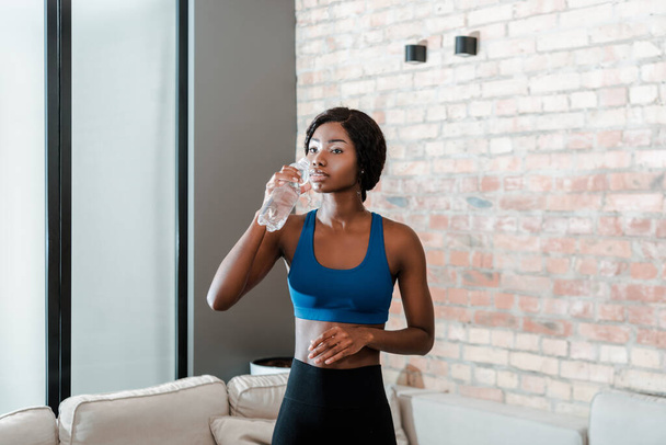 リビングルームで水を飲むアフリカ系アメリカ人のスポーツ女性 - 写真・画像