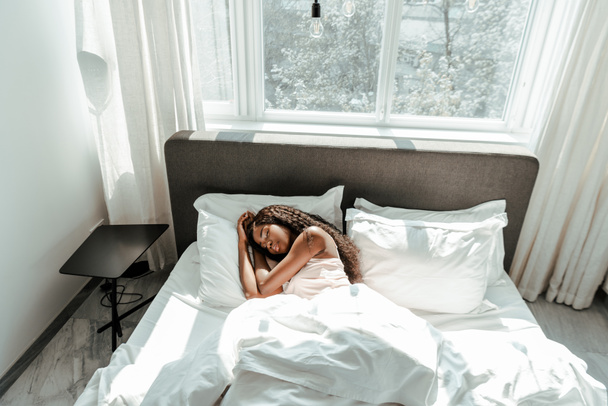 Vista de ángulo alto de la mujer afroamericana durmiendo en la cama en el dormitorio
 - Foto, Imagen