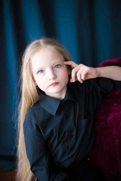 Cute little girl with long blond hair in a black shirt and jeans on a black  background in the studio - Valokuva, kuva