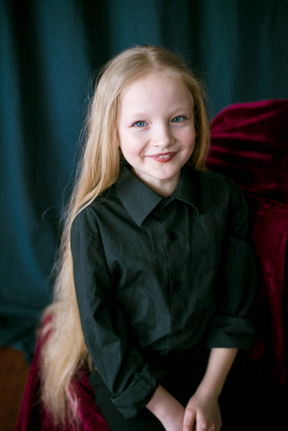 Cute little girl with long blond hair in a black shirt and jeans on a black  background in the studio - Фото, изображение