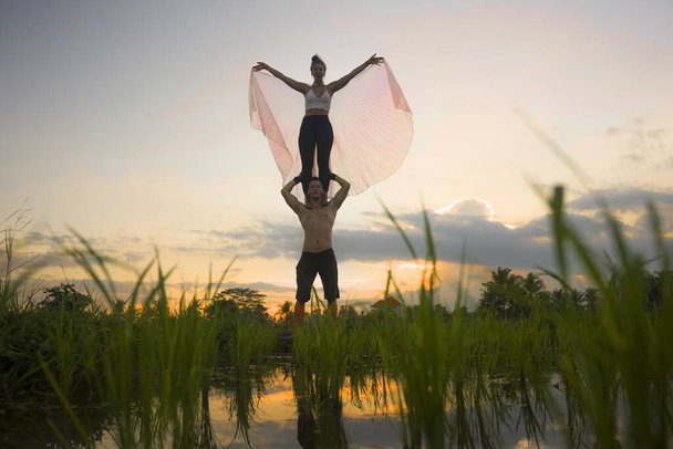 на открытом воздухе тренировки акройоги заката - молодая счастливая и здоровая пара практикующая акробатические упражнения йоги на красивом рисовом поле наслаждаясь природой и здоровым образом жизни, делая акробатическую позу
  - Фото, изображение