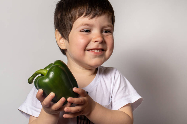 Küçük çocuk elinde yeşil biber tutuyor. Çocukların düzgün beslenmesi için. Çocukların diyetinde yeşil sebzeler. - Fotoğraf, Görsel
