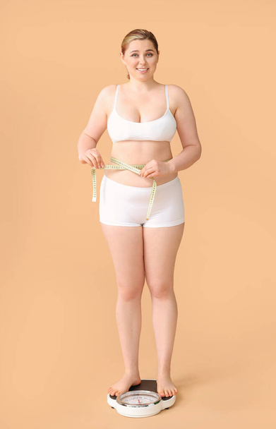 Mujer con sobrepeso de pie en escamas contra el fondo de color. Concepto de pérdida de peso
 - Foto, imagen