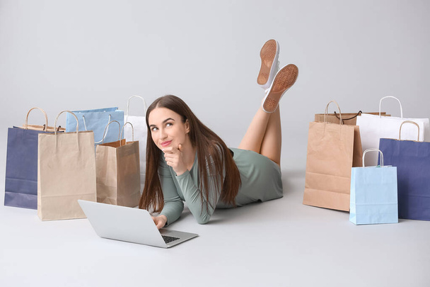 Mujer joven con portátil y bolsas de compras sobre fondo gris
 - Foto, imagen