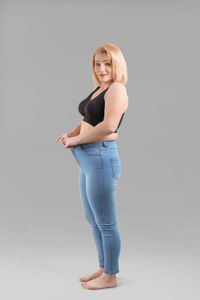 Übergewichtige Frau in lockerer Kleidung nach Schlankheitskur vor grauem Hintergrund - Foto, Bild
