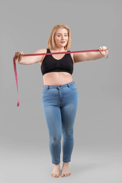 Overweight woman with measuring tape on grey background. Weight loss concept - Fotografie, Obrázek