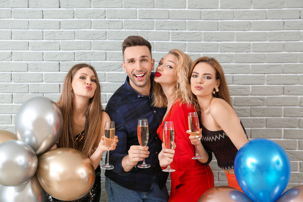 Счастливые люди с бокалами шампанского и воздушными шарами на кирпичном фоне
 - Фото, изображение