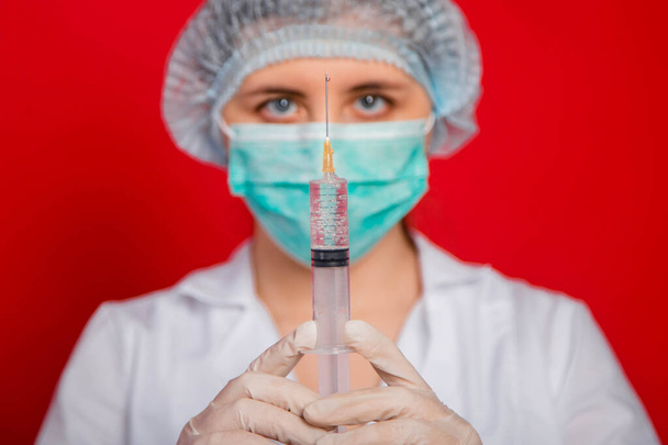 Κοντινό πλάνο σύριγγας με φάρμακο στα χέρια γυναίκας γιατρού σε κόκκινο φόντο. - Φωτογραφία, εικόνα