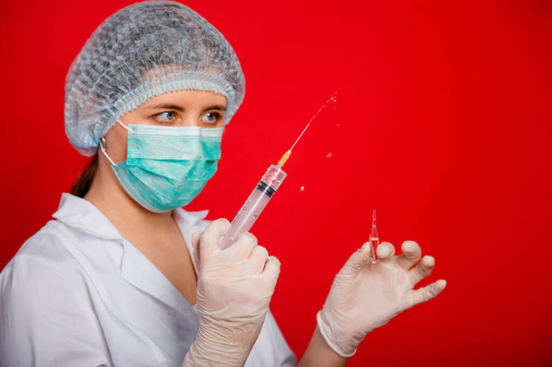 Close-up van een spuit met een stroom geneesmiddel van een naald in de handen van een vrouwelijke arts op een rode achtergrond. - Foto, afbeelding