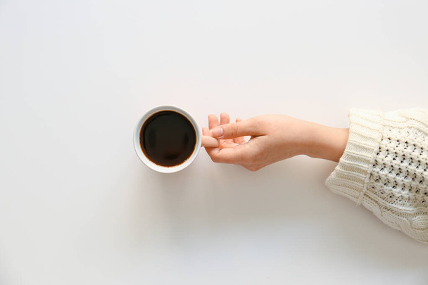 Жіноча рука з чашкою гарячої кави на світлому фоні, вид зверху
 - Фото, зображення