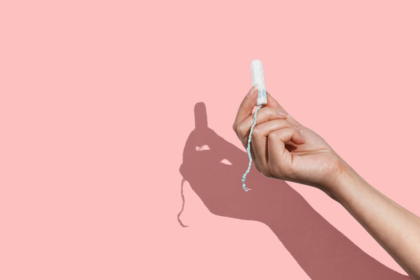 Womans hand holding a clean cotton tampon on the pink background - 写真・画像