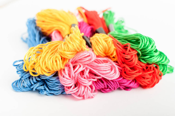 Muitos fios de costura coloridos vívidos misturados para bordados exibidos em um círculo isolado em uma mesa branca, vista lateral de matérias têxteis vermelhas, rosa, amarelas, azuis, pretas e verdes - Foto, Imagem