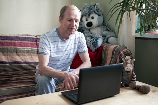 Hombre de mediana edad usando un ordenador portátil se sienta en casa en la mesa, en el sofá
 - Foto, Imagen