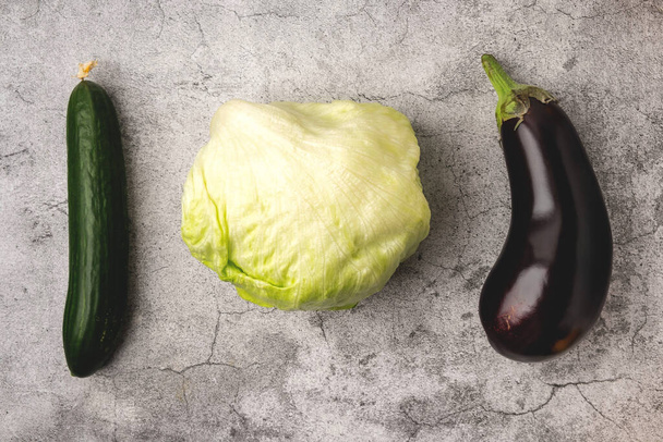 vegetables on a gray background: lettuce leaves, cucumber and eggplant, top view, copy space - Фото, изображение