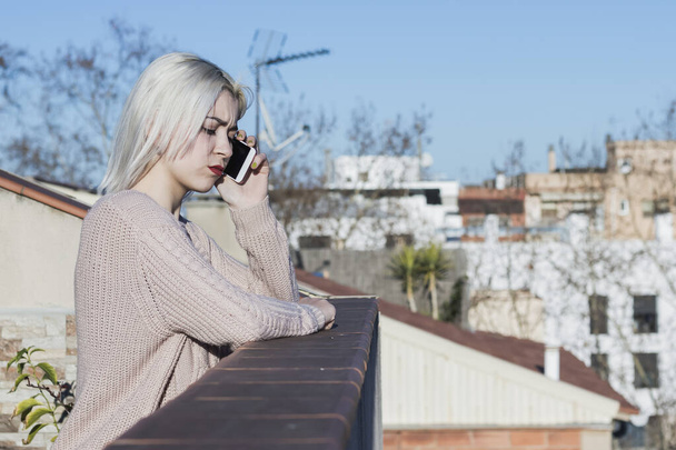 Girl talking on a smartphone while standing on the balcony. - Φωτογραφία, εικόνα