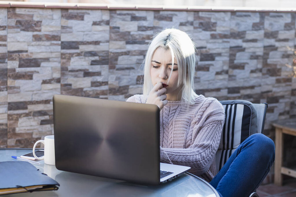 pensativo joven estudiante chica usando el ordenador portátil mientras se sienta al aire libre en casa terraza
. - Foto, imagen