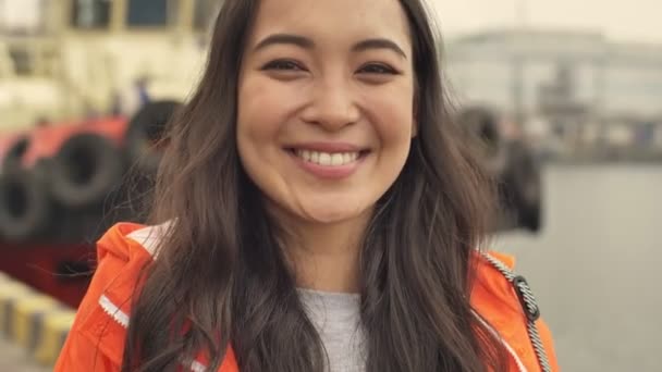 Pretty asian cheery positive woman walking by harbor grant outdoors in orange coat laughing. - Imágenes, Vídeo