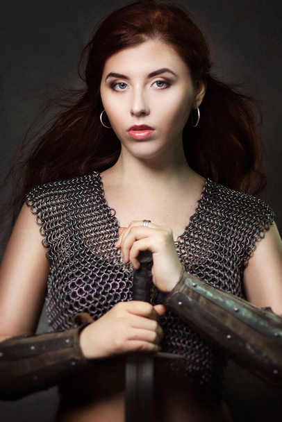 Beautiful girl warrior in chain mail with a sword in his hands. Medieval fantasy valkyrie with long hair posing on a dark background. - Fotoğraf, Görsel