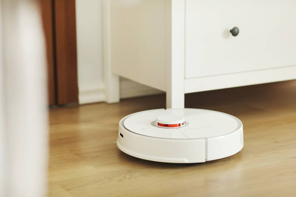 Robot vacuum cleaner performs automatic cleaning of the apartment at a certain time. white robot vacuum cleaner. home cleaning. Smart home. selective focus. - Photo, image