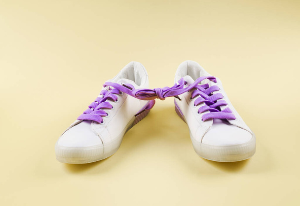 Белые кроссовки со связанными фиолетовыми шнурками на бежевом
 - Фото, изображение