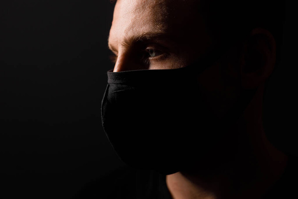 Handsome man in black t-shirt wear black medical mask, gray background. Coronavirus covid-19 quarantine period concept - Foto, Imagen