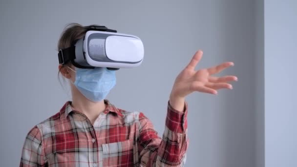 Nuori nainen yllään lääketieteellinen kasvonaamio ja virtuaalitodellisuus kuulokkeet - VR käsite - Materiaali, video
