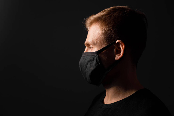 Handsome man in black t-shirt wear black medical mask, gray background. Coronavirus covid-19 quarantine period concept - Zdjęcie, obraz