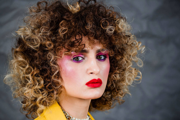 Portrait of a girl in a yellow jacket and blue jeans with afro hair of the eighties, disco era. Photo in studio on a gray background. - Photo, Image