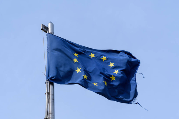 Romló európai uniós zászló, amely közvetlen napfényben fúj a szélben a tiszta kék ég felé, szakadt textilanyag - Fotó, kép