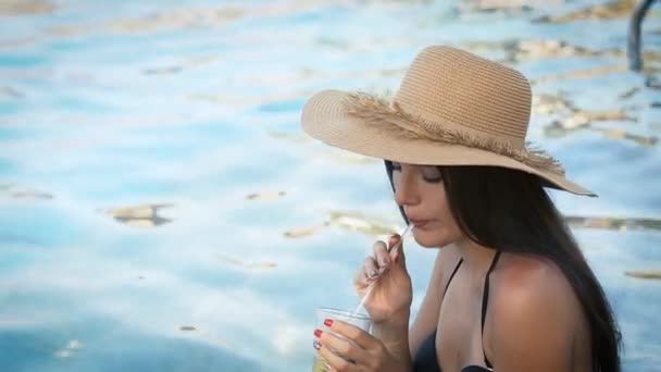 Woman in hat relaxing at pool with cosmopolitan cocktail - Materiał filmowy, wideo
