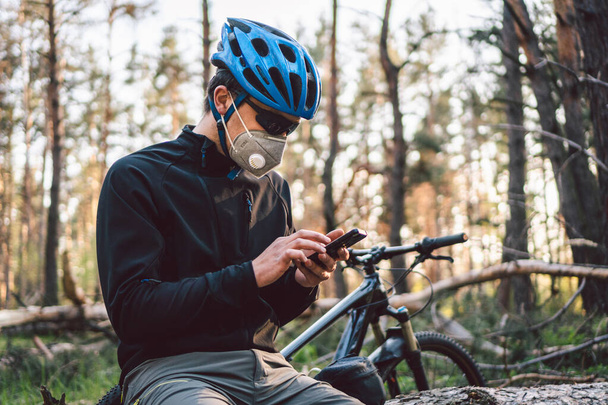 Cyclist wearing pollution mask in forest. Young guy in respirator with filter pm 2.5 with bike in park. Covid 19 Quarantine Sports. Flu epidemic, dust allergy, protection virus. Covid 19 virus concept - Фото, зображення