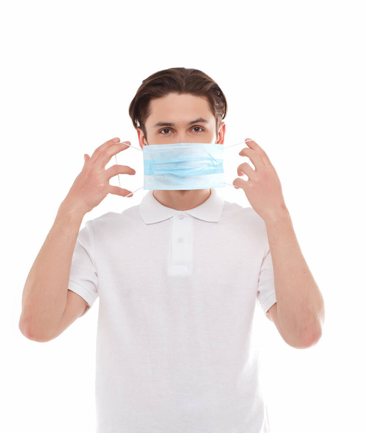 A man in a white T-shirt of European appearance puts on a medical mask. Isolated on a white background - Foto, Imagen