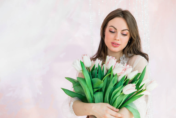 Attraente giovane donna che tiene in mano un mazzo di tulipani bianchi su uno sfondo rosa chiaro con posto per il testo, copiare lo spazio
. - Foto, immagini