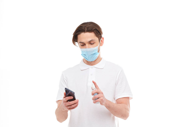 Een Europeaan met een masker desinfecteert de telefoon. Conceptuele foto over het thema van de covid-2019 pandemie. - Foto, afbeelding