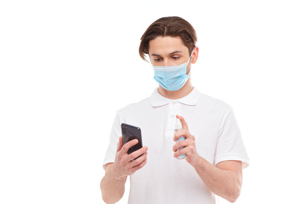 El hombre europeo enmascarado desinfecta el teléfono. Foto conceptual sobre el tema de la pandemia covid-2019
. - Foto, Imagen