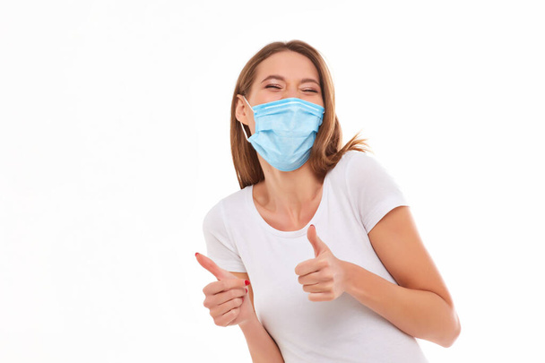 Европейская девушка в медицинской маске, показывает большой палец вверх. Концептуальное фото на тему пандемии Ковида 2019
. - Фото, изображение