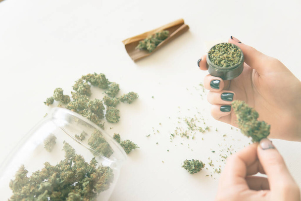 Woman preparing and rolling marijuana cannabis joint. Close up of marijuana blunt with grinder. Woman rolling a cannabis blunt on white background. marijuana use concept. Color toning - Fotó, kép