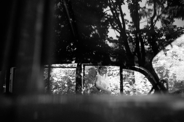 Наречений і наречений гуляють в саду біля рідкісного автомобіля. Весілля в лісі. Чорно-біле фото
 - Фото, зображення