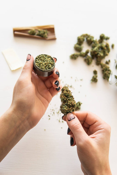 marijuana use concept. Woman preparing and rolling marijuana cannabis joint. Close up of marijuana blunt with grinder. Woman rolling a cannabis blunt on white background. - Foto, imagen
