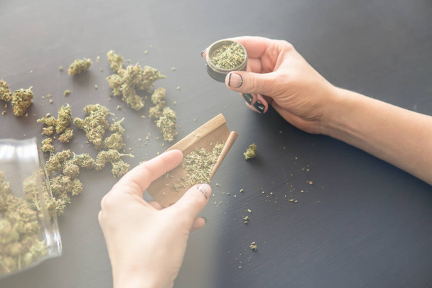 Close up Woman rolling a marijuana joint. Woman preparing and rolling marijuana cannabis joint. Close up of marijuana blunt with grinder. Pot use concept. Color toning - Фото, зображення